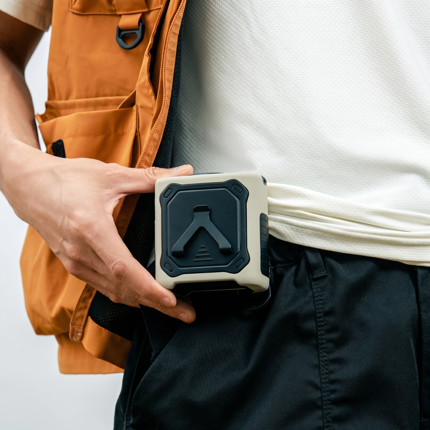 Person holding a small rectangular waist fan with a black and gray design, wearing an orange vest and white shirt.