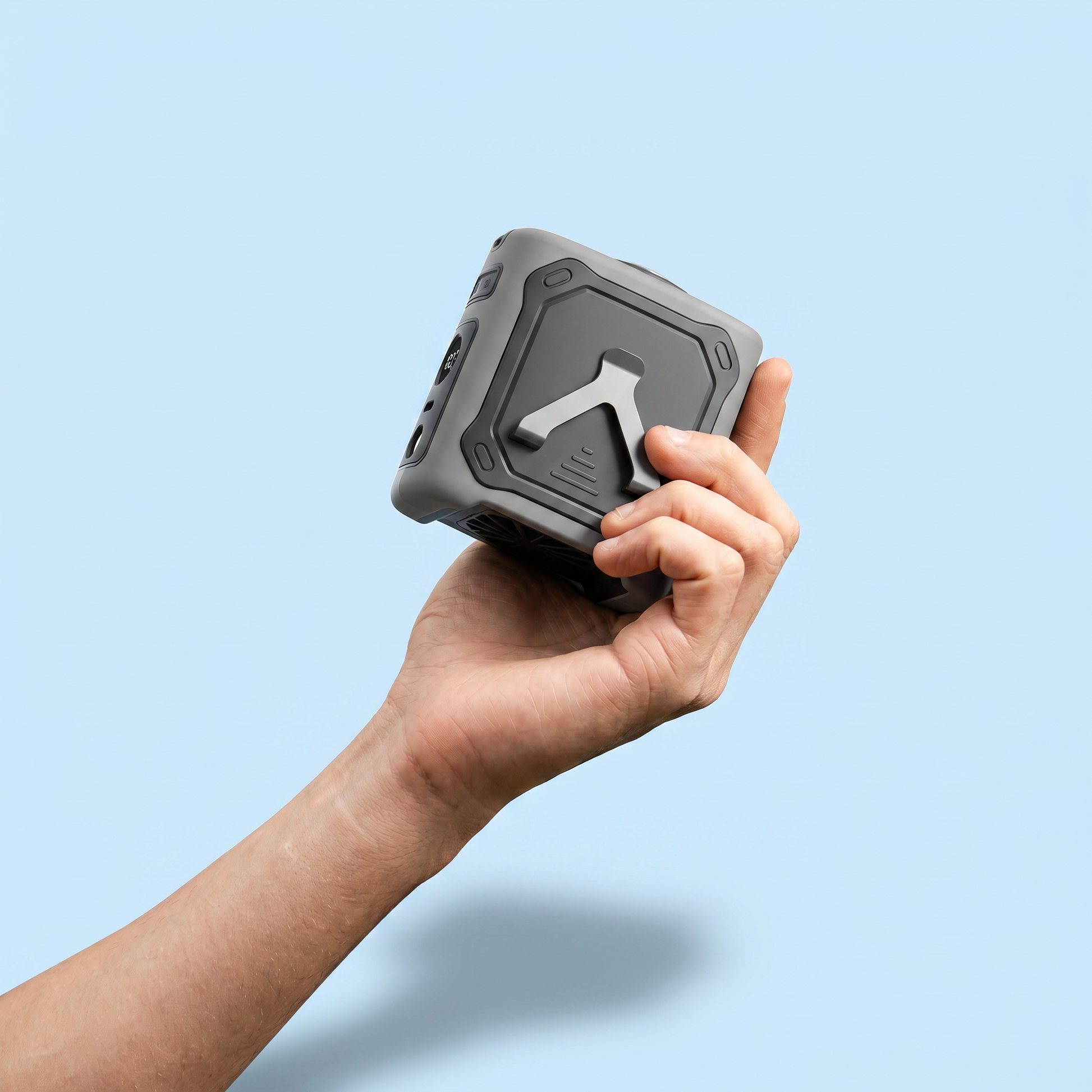 Hand holding a small, rectangular electronic waist fan against a light blue background